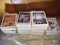 Three large stacks of magazines, predominantly Architectural Digest with one stack of Veranda magazines. Magazines are assorted issues mainly from 1970s to 2000s.