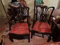 Pair of antique style wooden armchairs with reddish upholstered seats, shown in a dimly lit room.