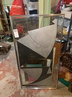 Frontal view of the framed abstract artwork showing full composition of large geometric shapes in black, white and gray under glass cover.