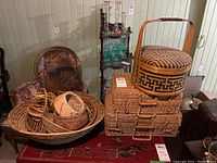 Wide view of assorted baskets including lidded baskets, picnic baskets, and assorted smaller woven baskets and trays, arranged on and around a wooden surface.