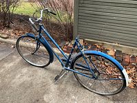 Full side view of the blue vintage Raleigh bicycle showing frame, tires, fenders, handlebars, and missing seat.