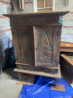 Front view of vintage Indonesian teak wood cabinet showing carved floral and geometric motifs on two doors and drawers below. Scratches and wear visible.
