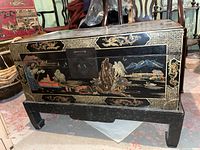 Front and side views of the chest showing detailed painted Asian-style landscapes, mountains, trees, villagers, and water scenes with a central metal latch plate.