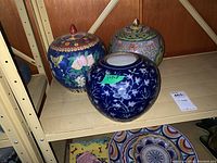 Three Chinese ginger jars on a shelf. One jar without lid has blue and white floral pattern.