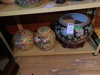 Shelf containing two smaller yellow ginger jars with lids and one large black ginger jar on a wooden stand