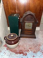 Full lot shot showing crock, clock, and green metal filing box against wooden wall on basement floor