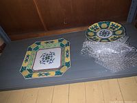 Photo of one large octagonal platter and a stack of smaller dishes with Asian style floral and geometric designs in green, yellow, and blue.