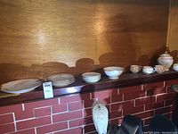 Photo of full Limoges china set displayed in a row including plates, saucers, cups, platter, bowl, and jar with lid on wooden shelf.