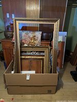Photo of box with multiple wood frames showing front of large gold-tone frame and tops of others inside the box