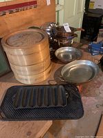 Overview of bamboo steamers, metal cake forms, roasting trays, and chafing dish with stand, and cast iron corn griddle.