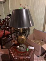 Full view of metal lamp with black lampshade on decorative wooden table, showing ornate base and brass accent.