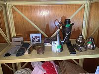 Shelf showing multiple metal items including jugs, coin holder, funnel, brushes, and figurines