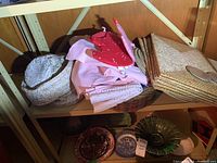 Shelf display showing woven wicker placemats, coasters, assorted pink and red linens, and a basket.