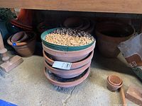 Stack of terracotta-colored ceramic planters with rocks in the top planter, showing cracks and weathering.