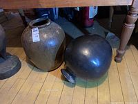 Photo showing both large vases on a wooden floor; one ceramic and one metal vase is lying on its side.