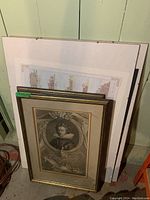 Three framed prints stacked against a wall, showing the edges and some frame details