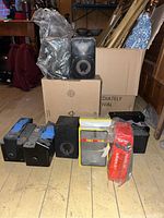 Overview of all speakers and some packaging items on wooden floor and cardboard boxes in background