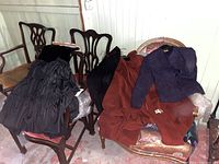 Photo of women's clothing including purple textured jacket, black dress, reddish-brown coats, hats, gloves laid on chairs.