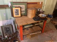 Overview photo of workbench showing wooden tabletop with items on top and framed artwork behind it.