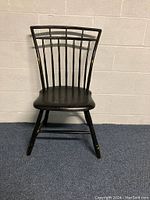 Full view of an antique black Windsor chair showing birdcage back design, wood seat, and overall condition including wear and distressing.