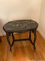 Full view of oval faux marble top end table from front corner angle against corner wall on wood floor.
