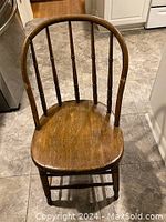 Fan back wooden chair made from oak or hickory, showing refinished surface and solid wooden curved seat with visible grain, joined legs and spindled backrest in a kitchen setting.