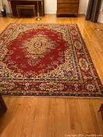 Top view of the Oriental style rug laid out on a hardwood floor showing intricate red and gold pattern and borders in very good condition with slight fringe wear.