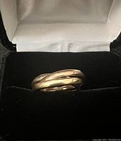 Three interlocking gold bands displayed in black velvet jewelry box, top view