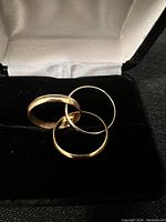 Three yellow gold band rings placed in a black velvet ring box with white satin interior.