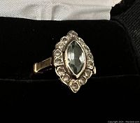 Close-up of the ring showing the marquise-cut aquamarine center stone surrounded by smaller round accent stones in a gold setting on a black background.