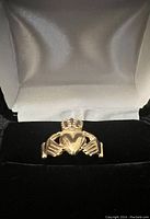 Front view of 14K yellow gold Claddagh charm ring in velvet jewelry box, showing heart with crown and two hands.