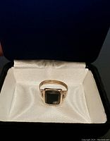 Front view of the gold ring with square black onyx stone in box with white interior.