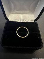 18 kt yellow gold band ring displayed on black velvet interior of ring box, showing top view of ring's smooth gold band.