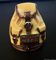 Front view of ceramic travel backpack trinket box showing yellow backpack with brown details and a Florida City 27 license plate.