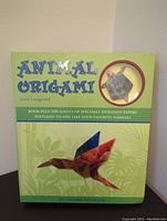 Front cover of the Animal Origami book showing title, author, and image of a colorful origami hummingbird on a green background with leafy design.