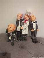 Front view of the four wine bottle holder figurines showing two butlers and a chef in formal attire, holding wine bottles in various poses.