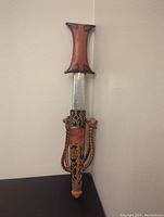 Ceremonial dagger with sheath, leaning against a wall, showing full length and handle details.