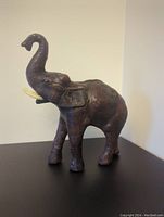 Front-side view of the leather elephant sculpture showing raised trunk and ivory-colored tusks.