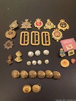 Full view of assorted military badges, buttons, buckles, and pins spread on a dark surface.