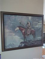 Full framed print hanging on a wall showing Aboriginal man on horseback with cloudy sky and rocks.