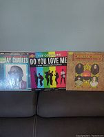 Front view of three vinyl albums side by side, showing covers of Ray Charles, The Contours, and The Mamas & The Papas albums on a sofa.