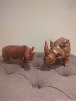 Photo of two wooden rhinoceros figurines positioned side-by-side showing front and side views on a textured surface.