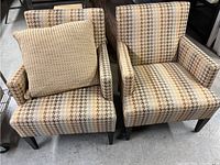 Front view of two fabric armchairs with geometric pattern upholstery in earth-tone colors and a large beige textured cushion on one chair.