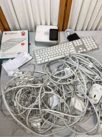 Full lot showing Mac mini, iPod, keyboards, mouse, tangled cables, and Logitech keyboard cover