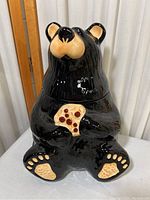 Front view of glossy black ceramic bear cookie jar holding a cookie, showing detailed snout, ears, and paws.