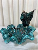 Front angled photo showing ruffled blue and light blue swirled glass ashtray with a dark blue bird perched on the rim.