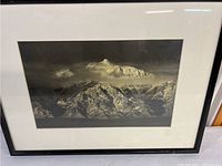 Photo showing Mount Everest framed print with white mat and black frame. View includes visible mountain peak, surrounding range, and dark sky background.
