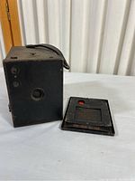 Side view of Kodak No. 2 Cartridge Camera next to No. 2 Hawk-Eye film cartridge on white surface.