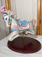 Front angle view of the Lennox porcelain carousel horse featuring pink, blue, and gold decorative accents and mounted on a dark wood base with a gold-toned pole.