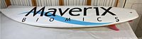 Full view of the white surfboard with Maverix Biomics branding on top side, showing overall shape and condition.